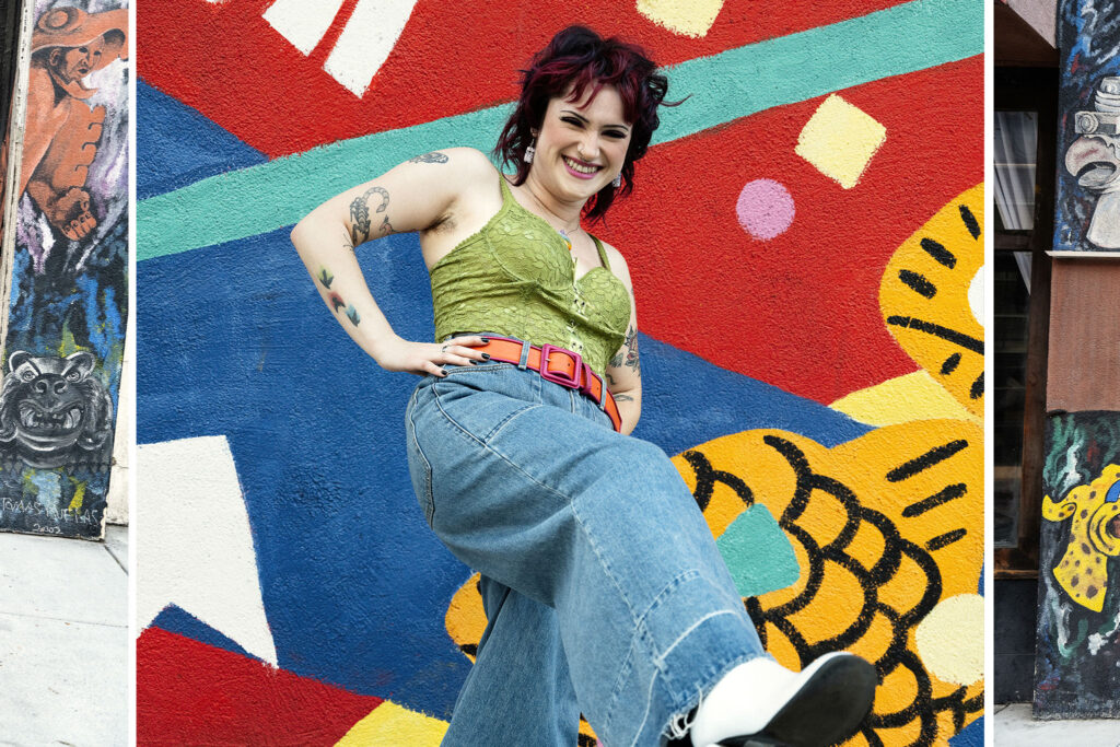 Sam wearing a green shirt and denim standing in front of a mural